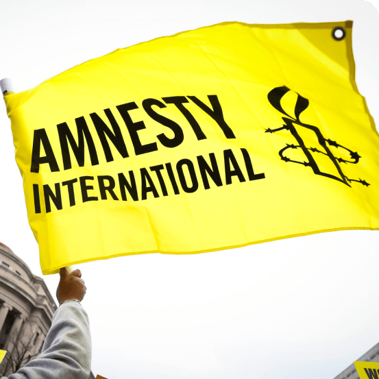 Jemand schwenkt eine gelbe Flagge mit einem schwarzen Amnesty International-Logo darauf